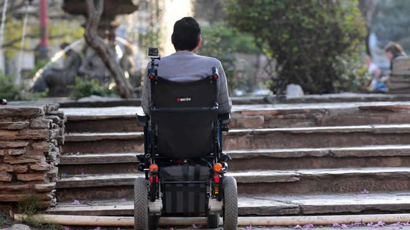 Home en cadeira de rodas fronte uns chanzos